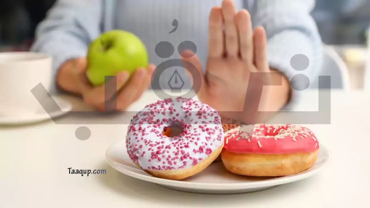 الصورة تحتوي على يد سيدة ترفض تناول الحلويات التي تتوي على السكر الصناعي وتستبدلها بالفواكة الطبيعية حث تمسك في اليد الاخري تفاحة خضراء